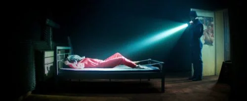Szenenbild aus Film Kidnapping Stella: Stella liegt gefesselt im Bett, der Entführer strahlt sie mit einer Taschenlampe aus der Entfernung an