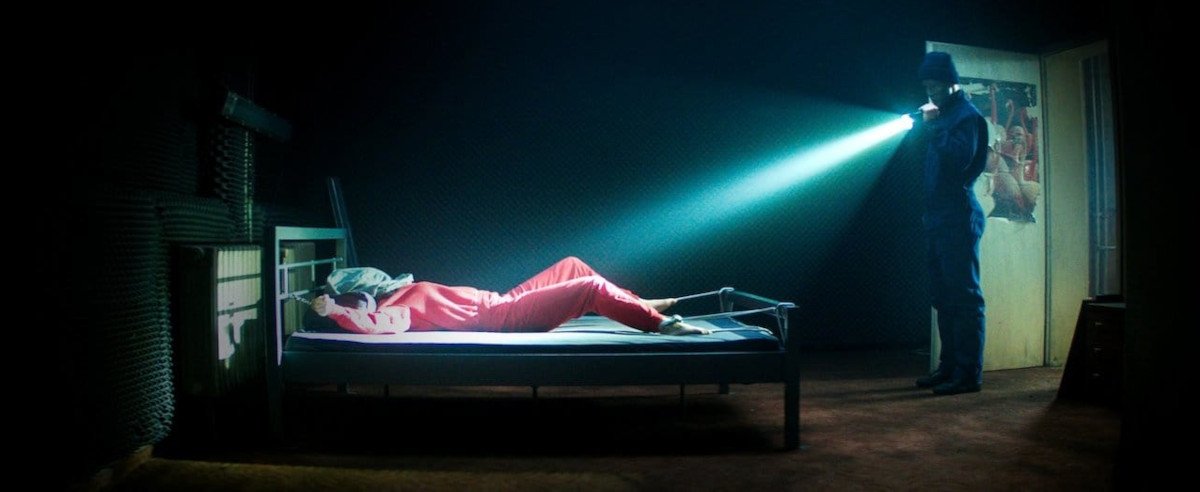 Szenenbild aus Film Kidnapping Stella: Stella liegt gefesselt im Bett, der Entführer strahlt sie mit einer Taschenlampe aus der Entfernung an