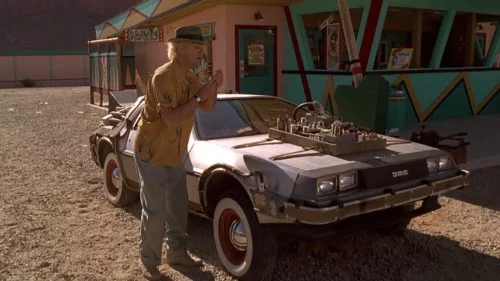 Doc Brown steht im Western fragend vor dem DeLorean