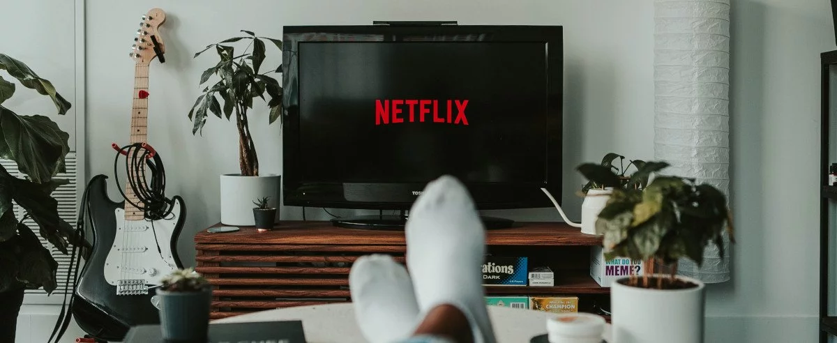 Ein Fernseher mit Netflix-Logo, davor zwei Füße auf einem Tisch beim entspannten Fernsehen