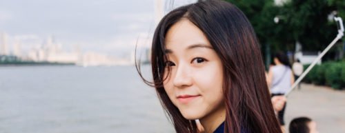 Eine Frau mit asiatischem Phänotyp befindet sich an einem Kanal und schaut direkt an die Kamera