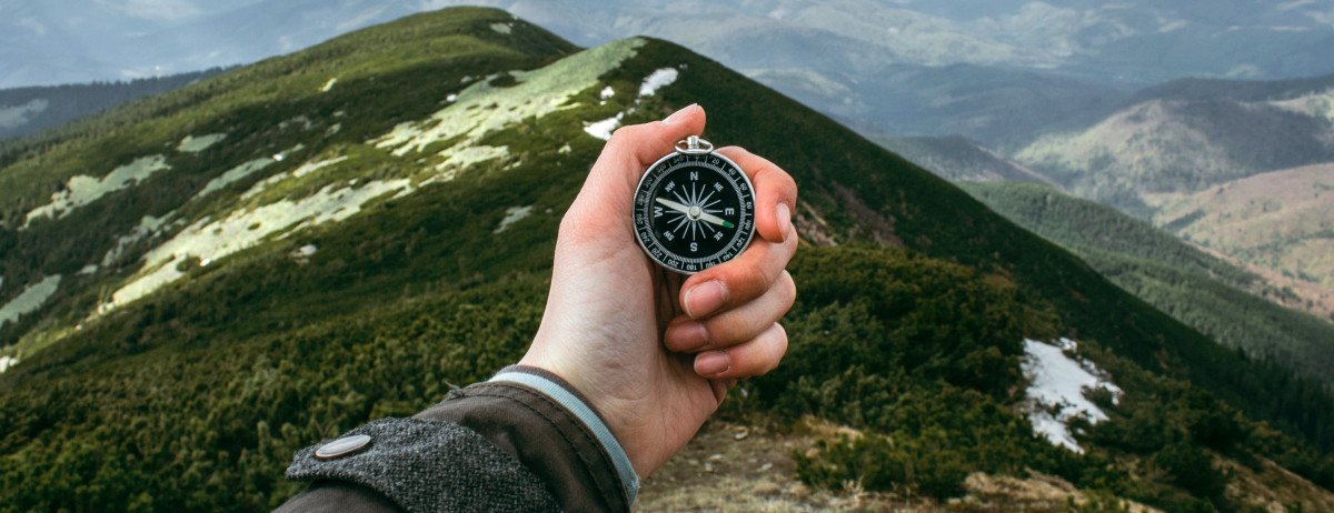 Eine Hand vor einem Bergpanorama. Die Hand hält einen Kompass.