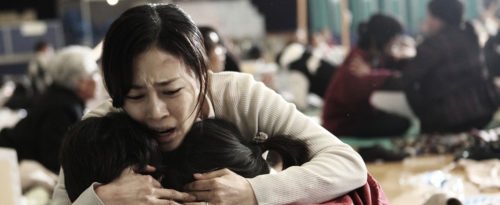 Eine Mutter kniet vor ihren Kindern und unarmt sie. Ihr Gesicht ist verzweifelt