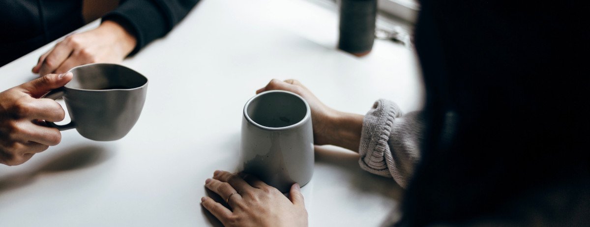 Zwei Personen unterhalten sich, nur ihre Hände sind zu sehen, wie sie Kaffeetassen festhalten