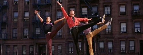 Drei Männer, die tanzen und dabei gerade ein Bein hoch in die Luft werfen