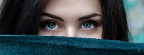 Eine junge Frau, die sich hinter einem Schal versteckt. Nur ihre Augenpartie ist sichbar