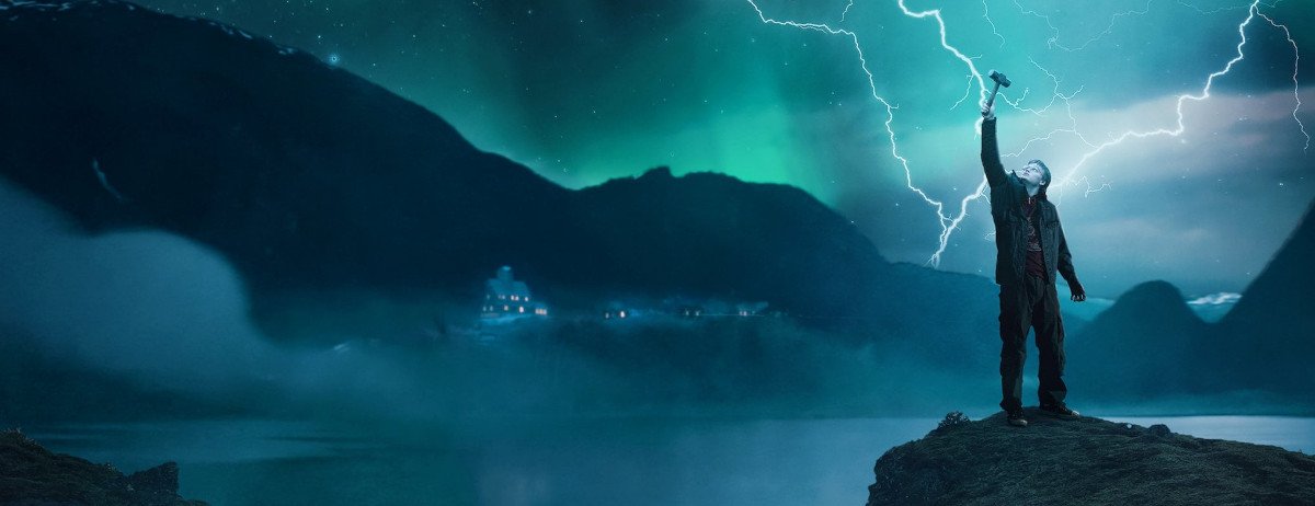 Der Hauptdarsteller hält auf einer Klippe Thors Hammer in die Luft, in den mehrere Blitze einschlagen