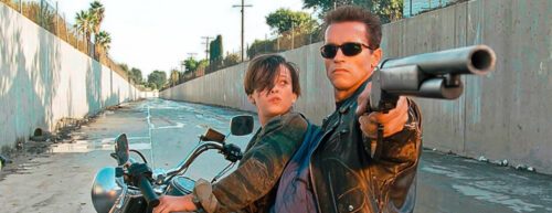 Der Terminator (Arnold Schwarzenegger) hält die Waffe auf den Zuschauer gerichtet, im Hintergrund John Connor (Edward Furlong)