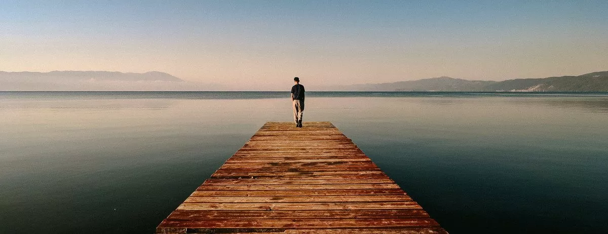 Eine Person allein auf einem Steg, schaut aufs Meer hinaus