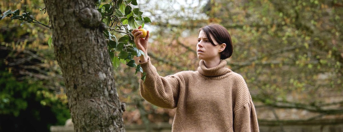 Jessie Buckley greift nach einem Apfel am Baum (Szenenbild aus Men)